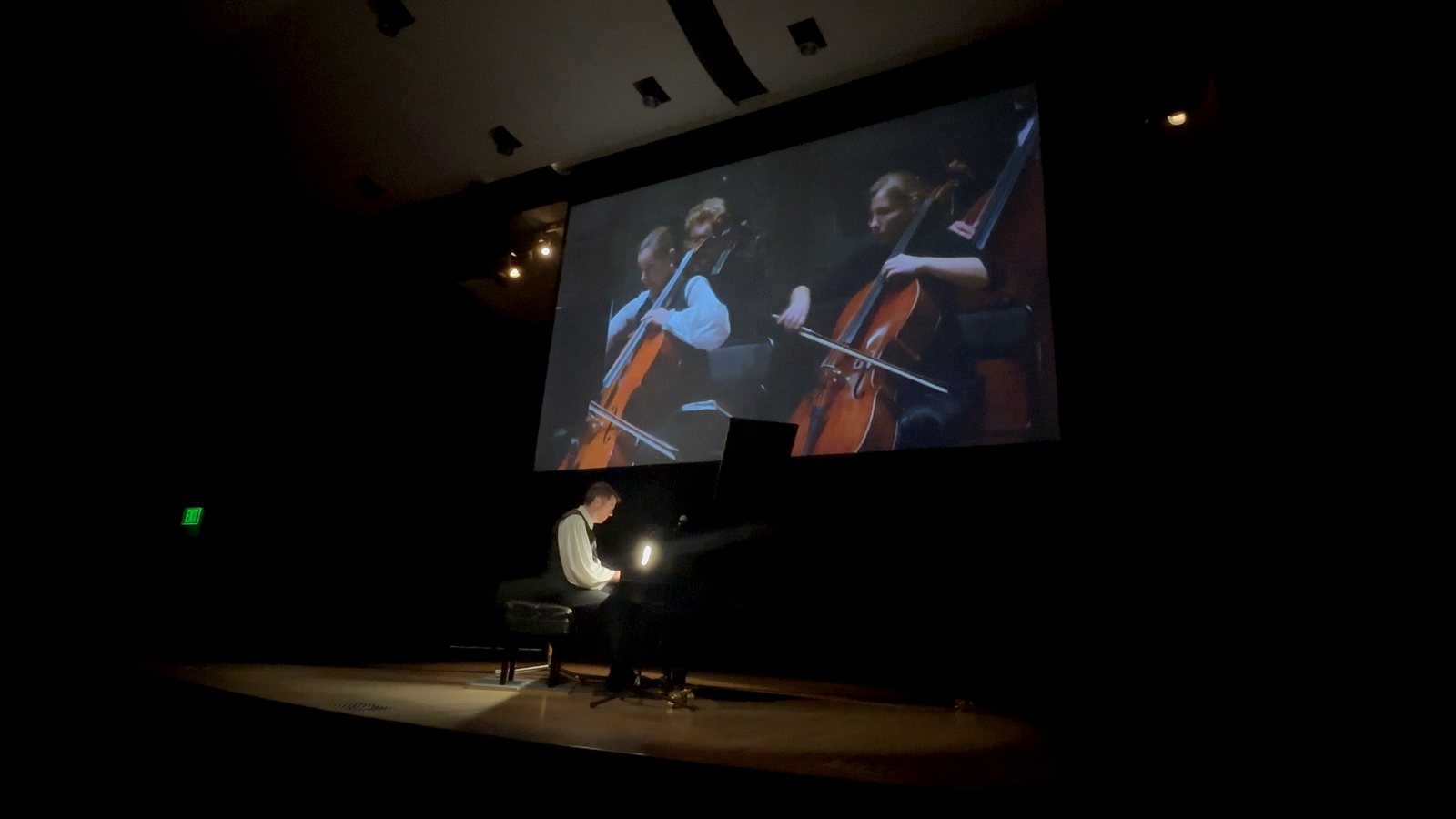 Calvin Jones at the piano with cellists projected on the screen above