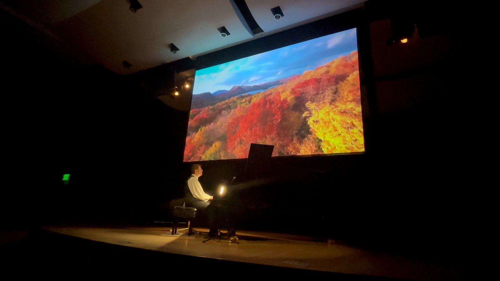 Calvin Jones performing as autumn mountain scenery plays on the screen behind him
