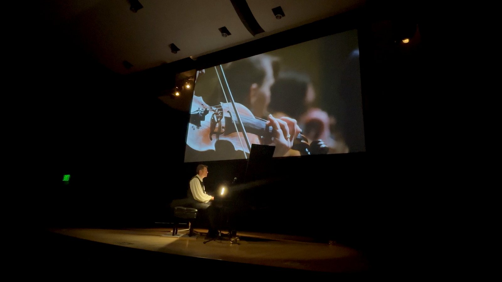 Calvin Jones performing with a close-up of a violinist on the screen behind